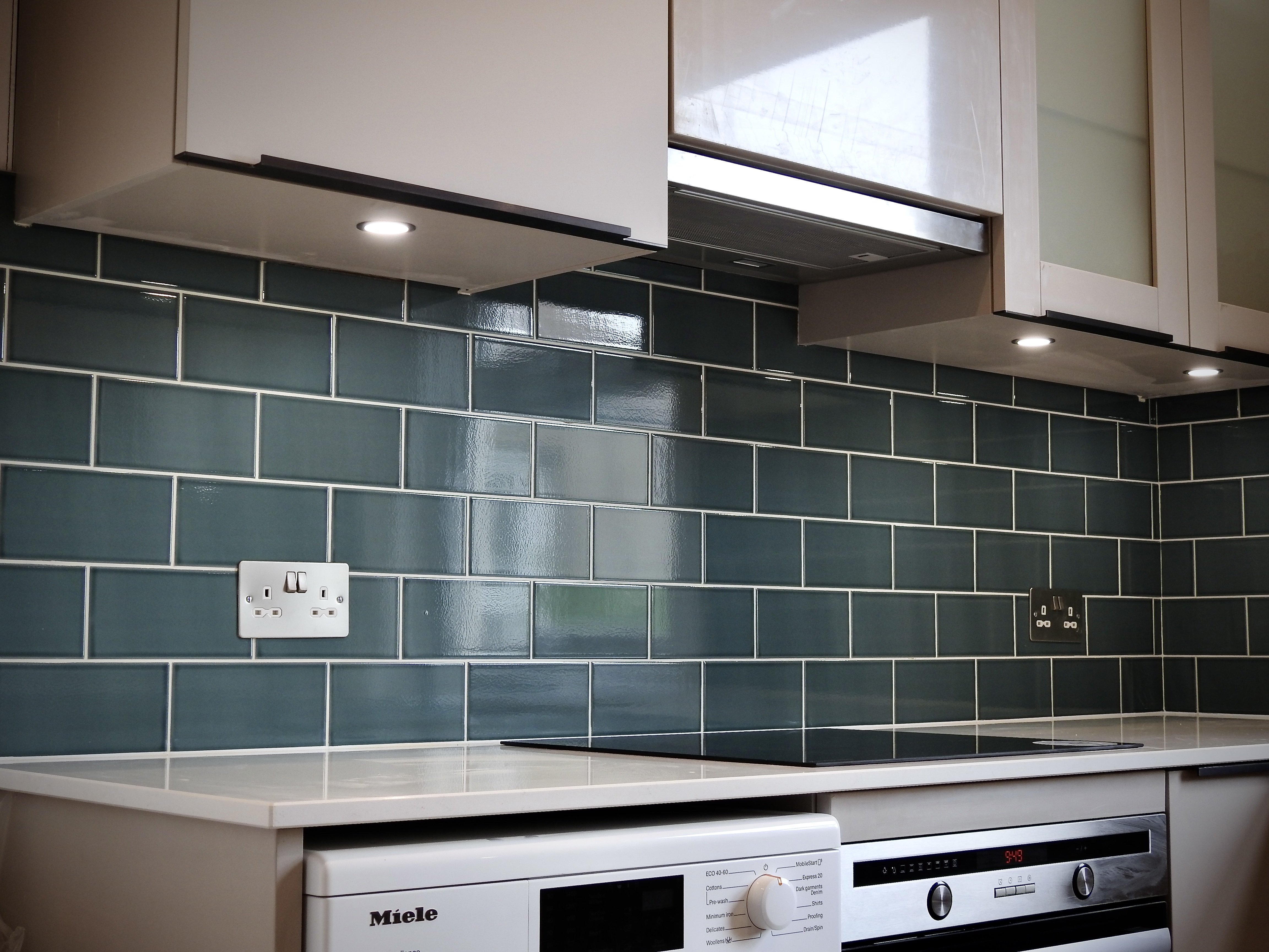 Kitchen fitted in Hove with blue metro style tiles, white grout, white marble work surface and spot lights under the cupboards. 