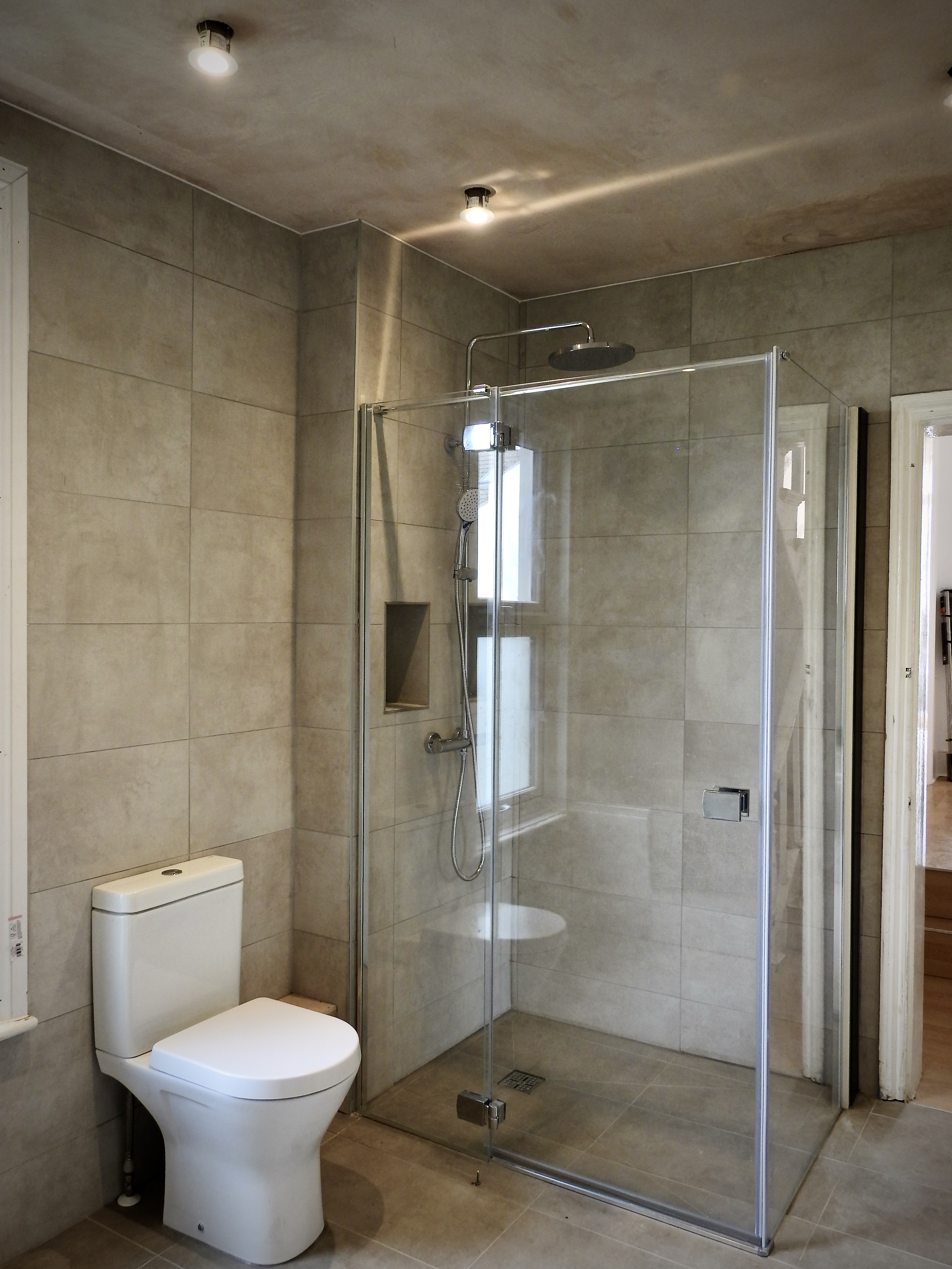 Bathroom Fitted in Hove with wet-room style tiled floor, drench shower and beige tiles. 